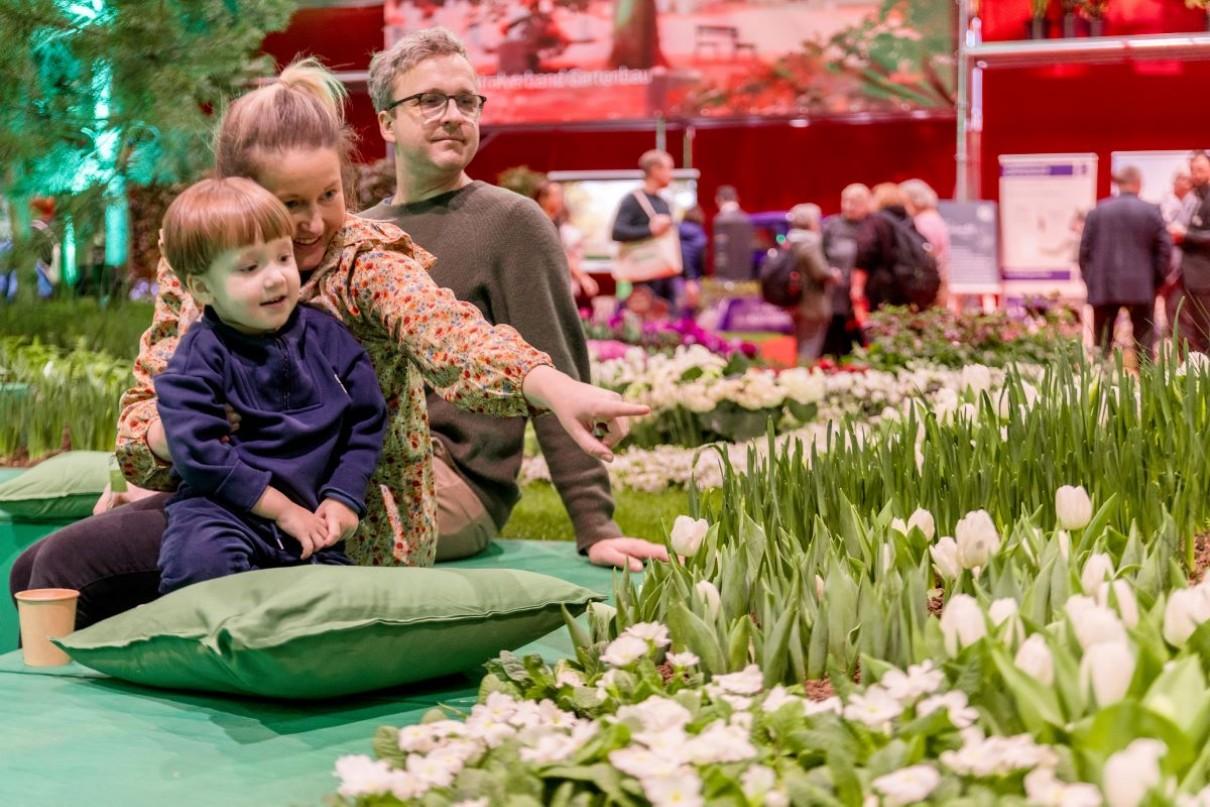 Mutter und Vater sitzen mit dem Kind vor einem Tulpenfeld und zeigen auf die Blumen