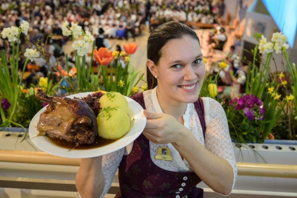 A woman holds a plate with meat and dumplings, in the back you can see flowers.