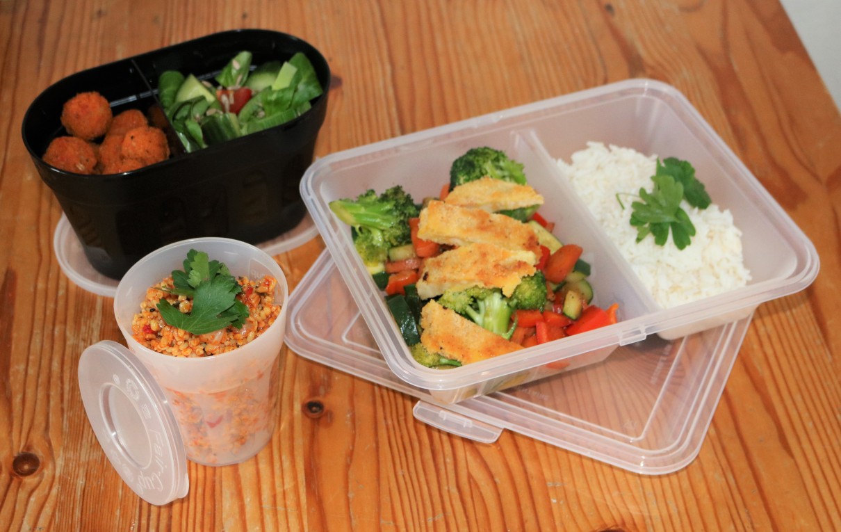 Ein Bild zeigt drei Lunchboxen, die mit Reis, Salat und weiteren Gerichten gefüllt sind.