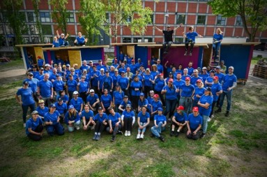 100 Messe Berlin employees sit in front of 5 built Tiny Houses for homeless people