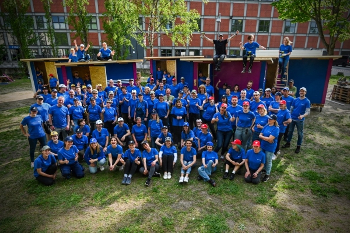 100 Messe Berlin Mitarbeiter sitzen vor 5 Tiny Houses für Obdachlose
