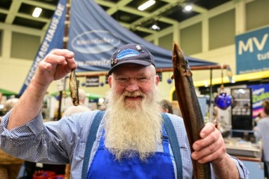 Man with white beard holding smoked fish in his left and right hand.