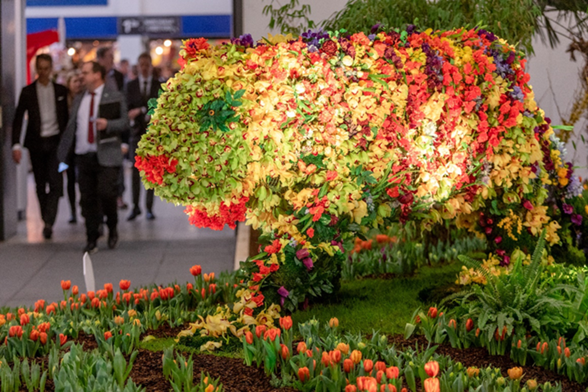 A big cat made of flowers in the flower hall, with visitors to the Grüne Woche in the background.