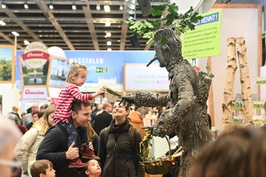 Child on his father's shoulders shakes hands with man in tree costume