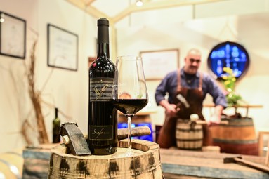 Eine Flasche Rotwein und ein Weinglas stehen auf einem Holzfass