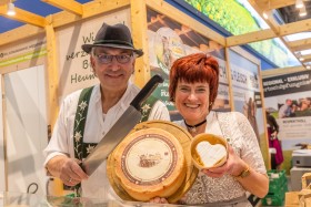 A couple from Bavaria holding a loaf of cheese to the camera.