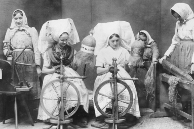 Frauen in Tracht beim Arbeiten am Spinnrad.